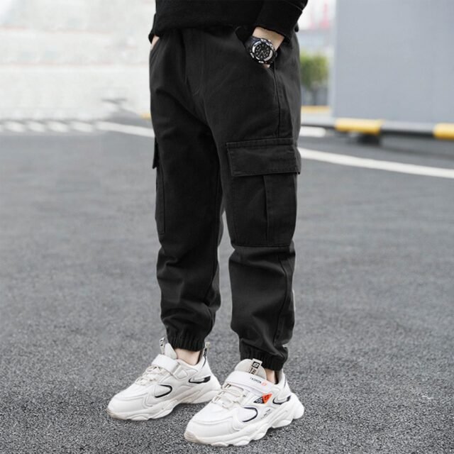 Boy in black cargo pants and white sneakers standing on pavement.